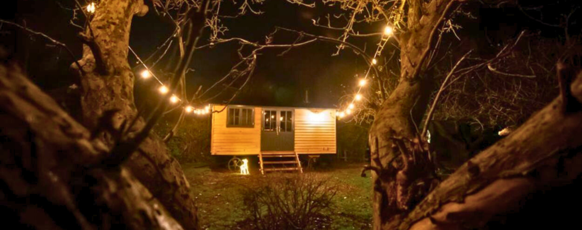 A shepherd's hut at night surrounded by fairy lights.