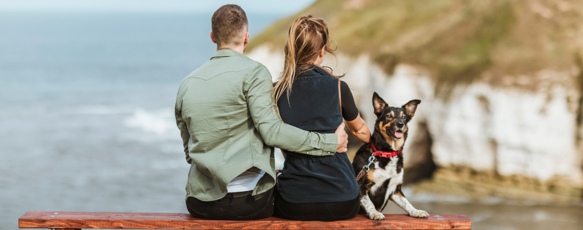 A couple sat on a bench looking out across the sea and chalk cliffs at Flamborough, with their black and white dog by their side.