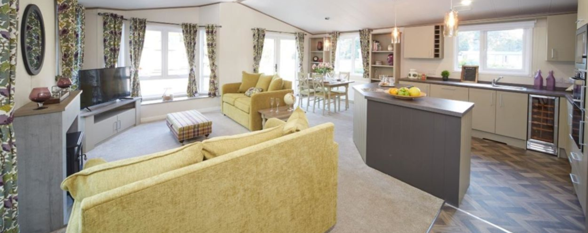 The inside of some of the accommodation available at South Cliff Holiday Park in Bridlington. An open plan kitchen, dining space and living room with green sofas.