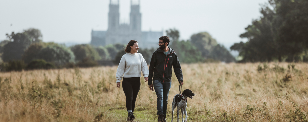 A couple walking their dog on Beverley Westwood with the silhouette of Beverley Minster in the distance