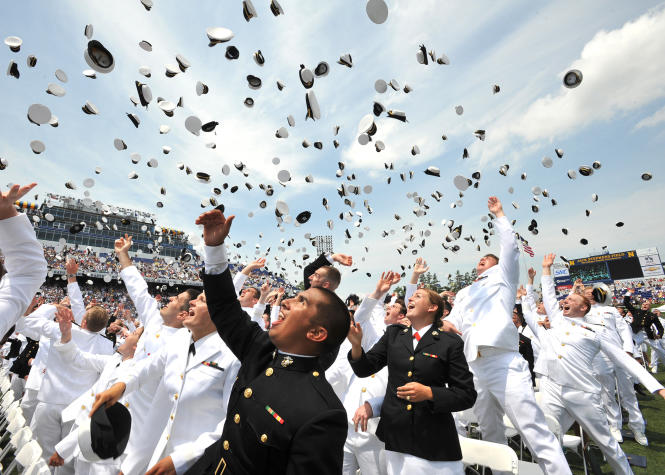 A group of men and women throw their hats in the air upon graduation from the Naval Academy.