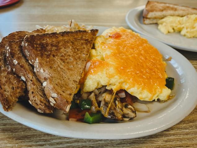 An omelet stuffed with vegetables and topped with melted cheese sits next to pumpernickel toast on a plate at Dig-in Cafe.