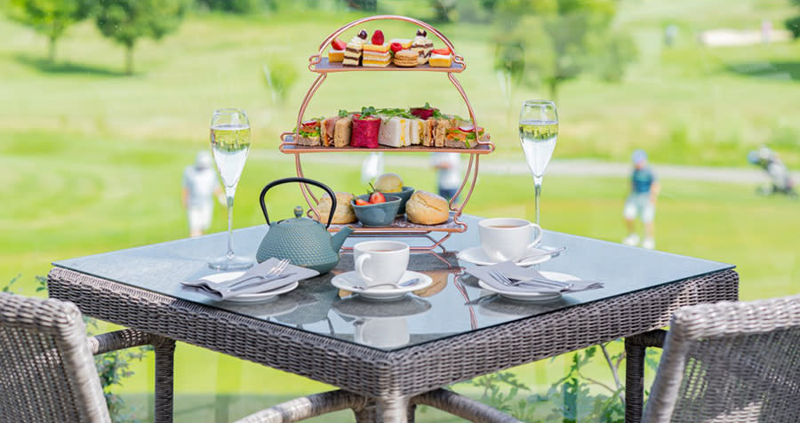 Afternoon tea set up on the terrace at Tewkesbury Park with golfers in the background