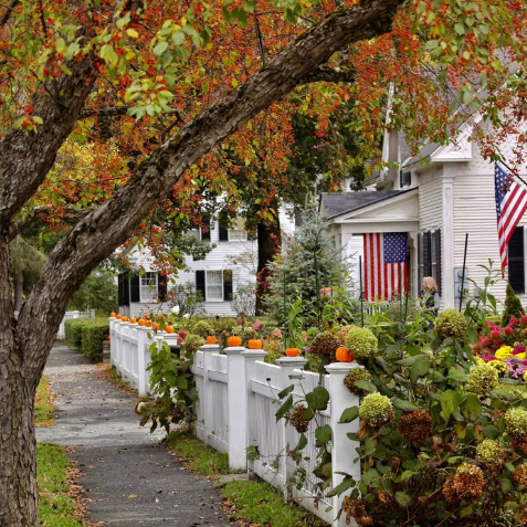 Woodstock VT street during fall foliage with pumpkins on a white fence and American Flag hanging on house