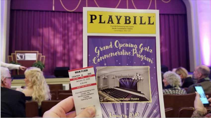 A hand holding a playbill and a ticket in front of the stage