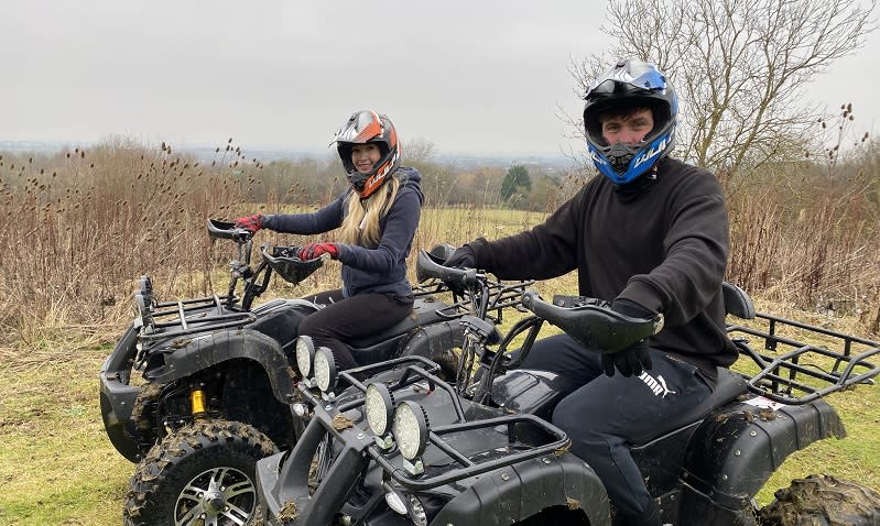 Two people sit on quad bikes in the countryside