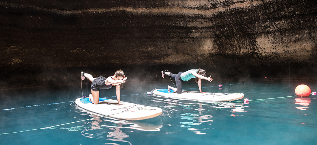 Two women on paddleboards doing yoga in a natural crater