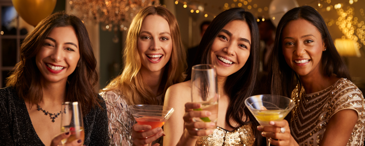 Four women pose with cocktails in an advertisement for the 12 Drinks of Christmas event at Exploration Place