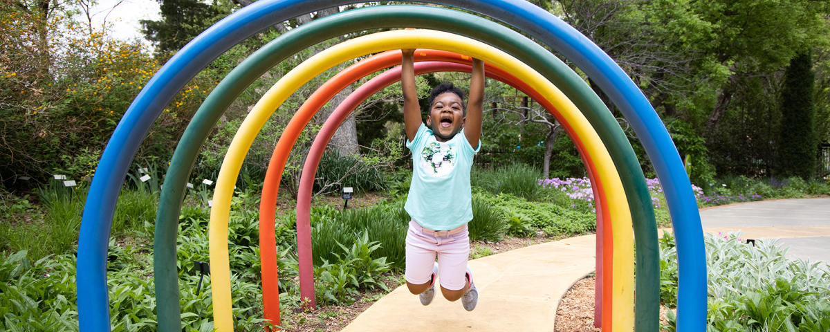 A girl hangs from a rainbow sculpture at Botanica Wichita.