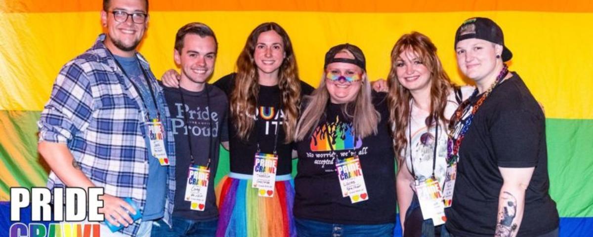 Six people pose in front of a Pride flag
