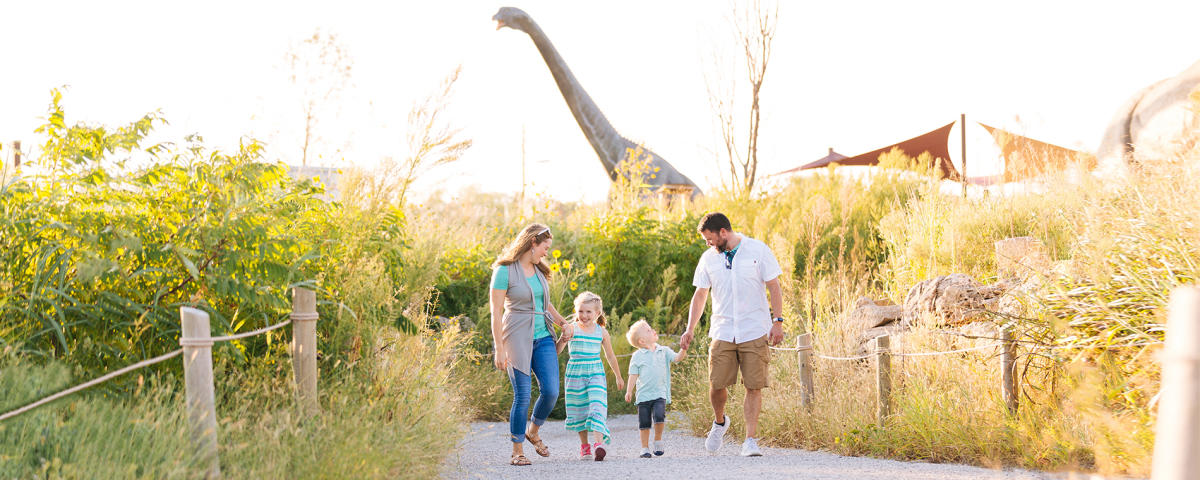 A mother and father walk hand-in-hand with their son and daughter along a path at Field Station: Dinosaurs