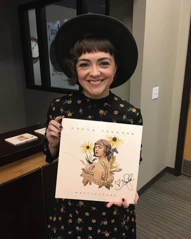 Artist Neyla Pekarek holds up a signed album with the artwork for her album Rattlesnake