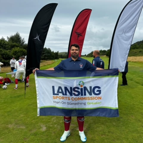 A footgolf player holds up the Lansing Sports Commission sign at a tournament in Scotland.