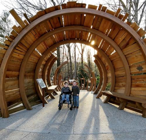An image of two children under an arching wooden tunnel at the State Botanical Gardens of Georgia. One child is in a wheelchair.