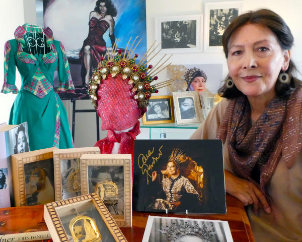 Nina Khan standing next to items from her Ava Gardner Collection including the golden crown from The Blue Bird, pictures, artwork and a reproduction of a Show Boat costume