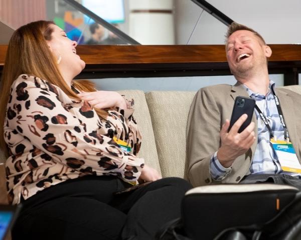 Two colleagues share a laugh while sitting on a couch.