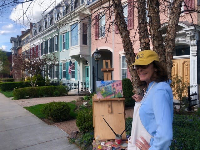 Woman painting color row houses on canvas easel