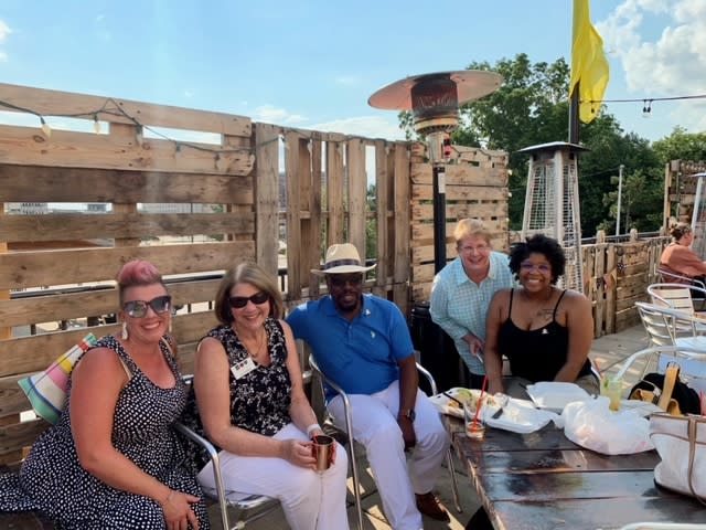 A group of adults sitting together and posing for a photo outside of a local bar.