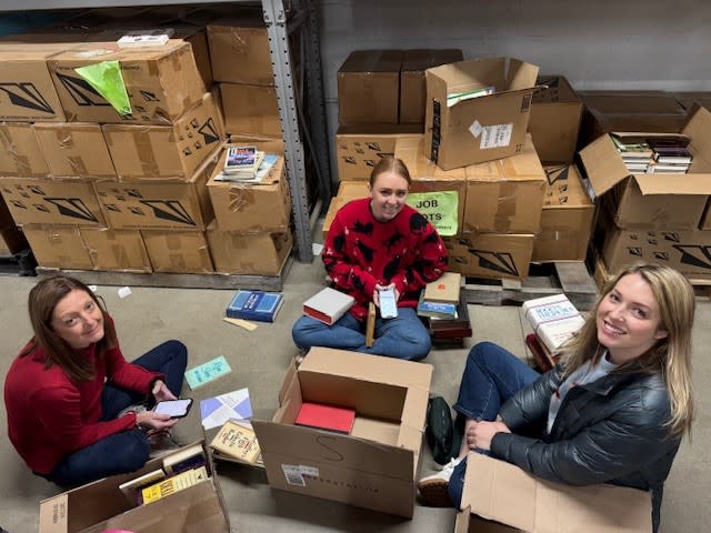 Three women sit on the floor sorting through books
