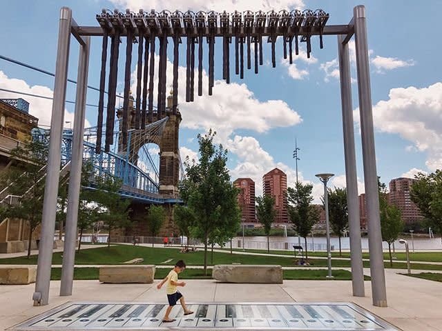 photo of a little boy  in a yellow shirt walking across a foot paino at smale riverfront park in cincinnati oh