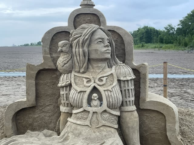 Sand sculpture of a woman looking off into the distance. A bird sits on her shoulder and she is wearing armor made out of what appears to be bird cages.