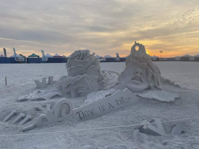 Sand sculpture of two half-melted faces with a banner next to them reading "Time Is A Killer"