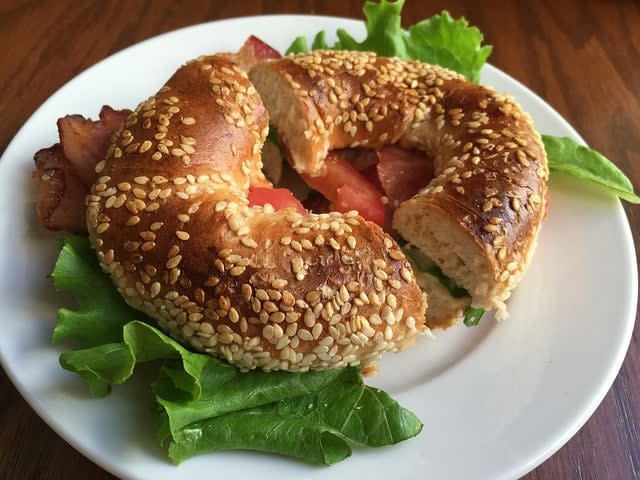 Sandwich on sesame bagel wit leafy lettuce on a white plate