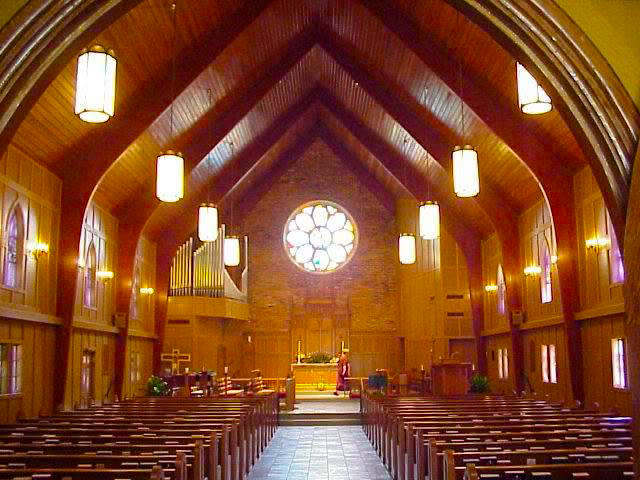 Interior of Christ Episcopal Church in Covington, with rows of wooden pews beneath a vaulted wood ceiling, stained-glass windows and a large rose window above the altar.