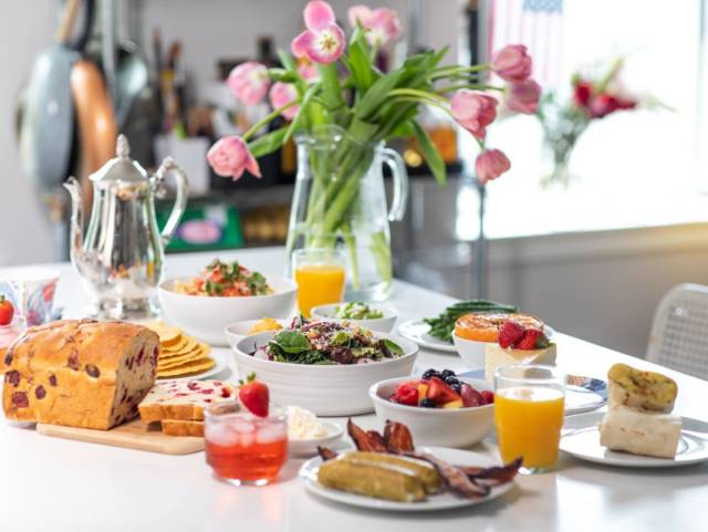 Various brunch plates, oragne juice, pink cocktails, tea pot, and flowers