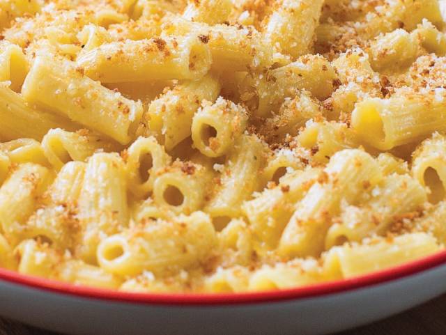 Creamy baked mac n' cheese with bread crumbs placed on a white plate with a red trim