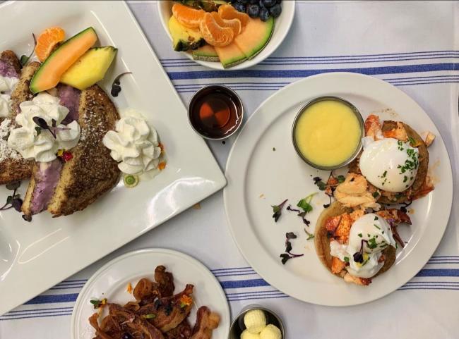 Owl's Nest Resort - Mother's Day Brunch (Eggs Benedict, fresh fruit, bacon, French Toast on plates set on top of white and blue striped tablecloth)