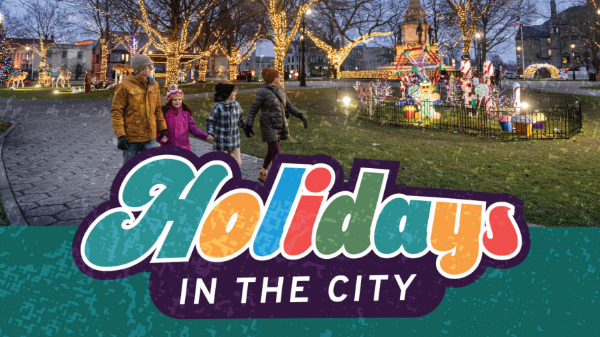 Promotional banner for 'Holidays in the City' featuring a group of people walking in a festive, decorated outdoor Hackley Park with holiday lights and displays during evening.