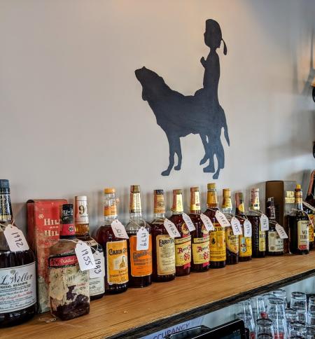vintage bourbon selection at libbys southern comfort in covington ky including several bottles of bourbon on a shelf with a logo silhouette of a dog and little girl on the wall