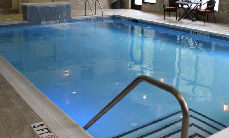 Indoor hotel pool with warm lighting and a small waterfall feature, perfect for families visiting Fayetteville, NC.