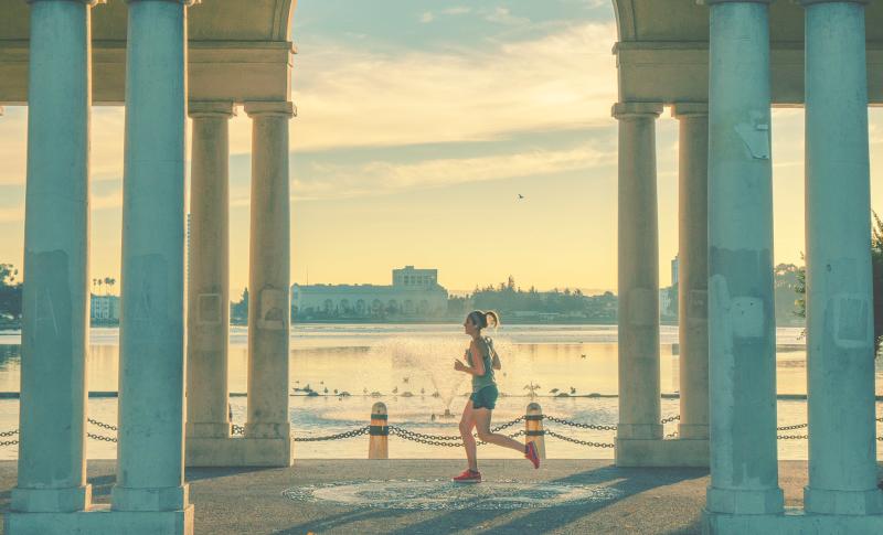 A woman jogs past ancient columns, illuminated by the warm hues of a sunset.