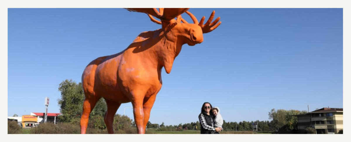 Woman And Child Standing By Orange Moose in Black River Falls, WI