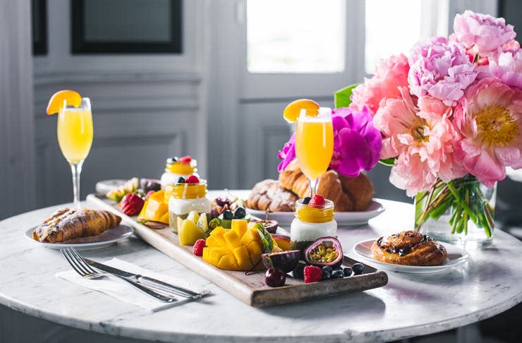 Two mimosas, pastries and fruit with a bouquet of pink flowers from The Blue Hen in Saratoga Springs