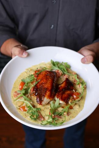hands holding a white plate with sauce and a piece of chicken on top