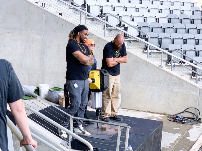 Three people practice leading the Jackhammer Celebration at Lower.com Field