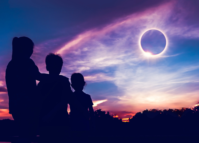 Image is of a woman with two kids as they face a full solar eclipse.