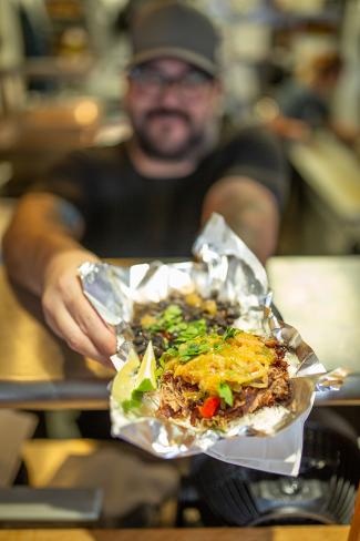 bearded man holding out a street taco in foil