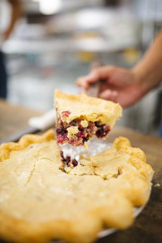 A hand lifting a piece of pie from the pie pan