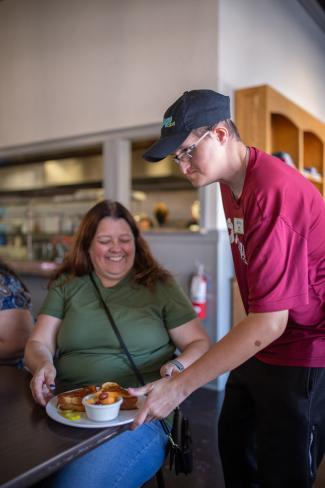 woman in green shirt sits at table where server is serving her a plate of food