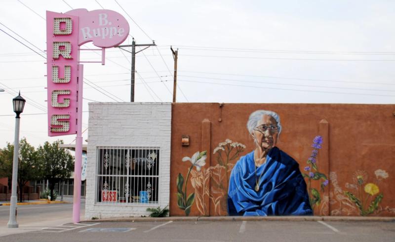 View of the Nani Chacon mural depicting healer Maclovia Zamora, on the farside of the historic B. Ruppe pharmacy. The classic neon sign is bubblegum pink.