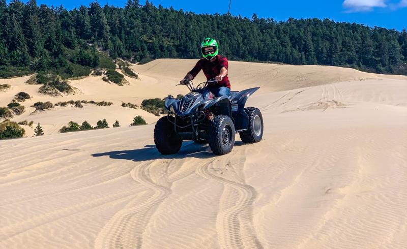 ATVs on the Oregon Dunes by Melanie Griffin A man sits on an ATV on top of a large sand dune with forest in the background.