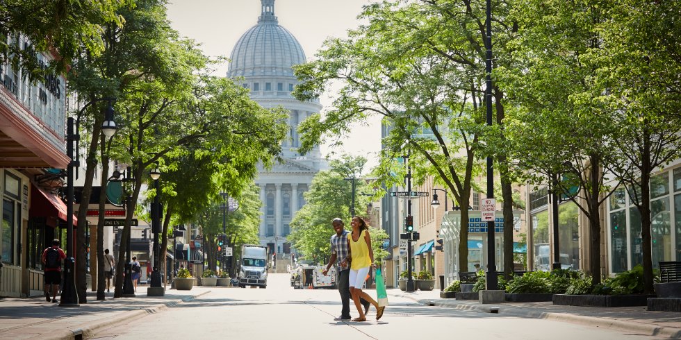 A couple walks across State Street in downtown with the Capitol Building in the background