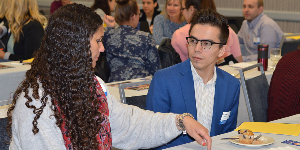 A young man and young woman have a one-on-one discussion while others chat in the background
