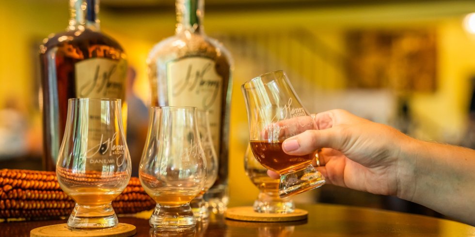 A person holds a small glass of bourbon as part of a bourbon flight at J. Henry and Sons Distillery