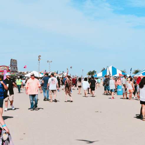 A crowd of people walking along the beach with carnival tents