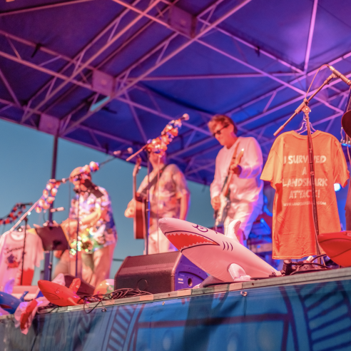 A band performs on a brightly-lit stage decorated with leis and inflatable sharks